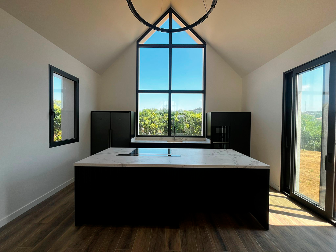 Cocina negra con isla central y campana extractora de encimera oculta frente a ventana catedral.
