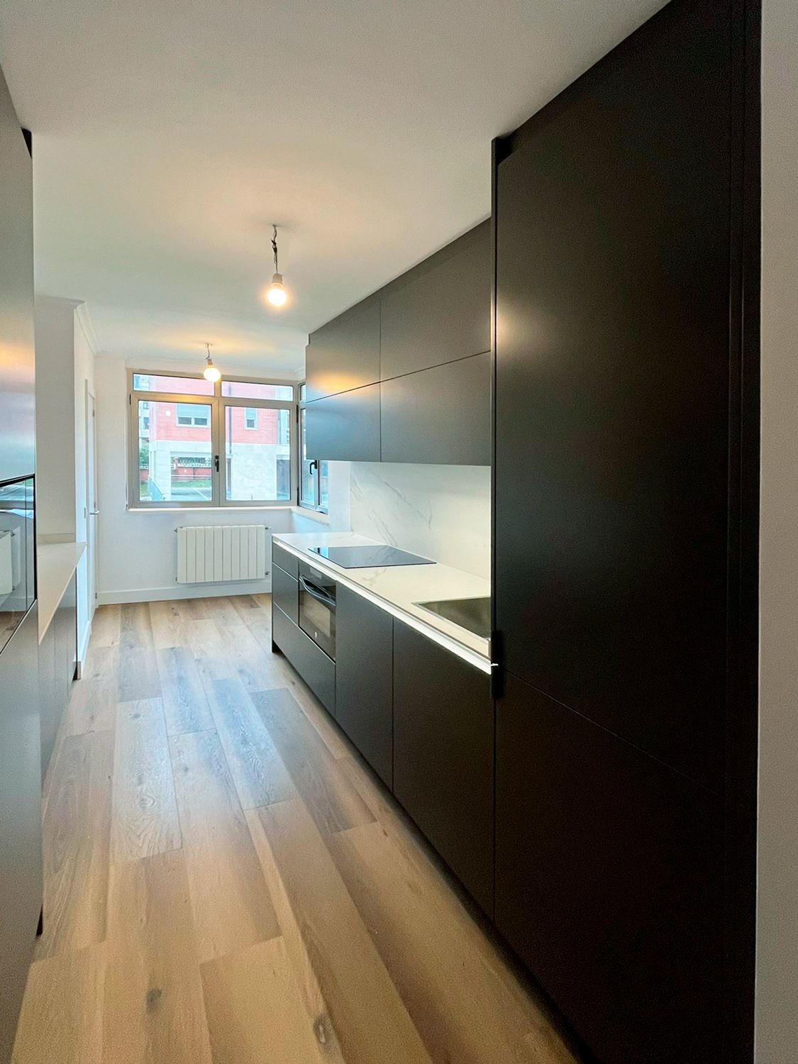 Detalle de cocina negra con encimera blanca y muebles altos lisos