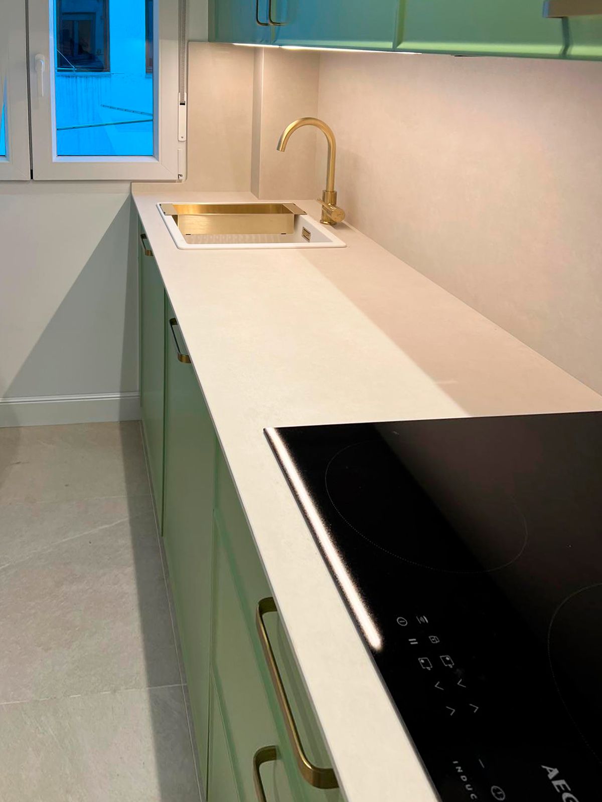 Cocina verde con tiradores dorados y encimera porcelánica clara Soinco