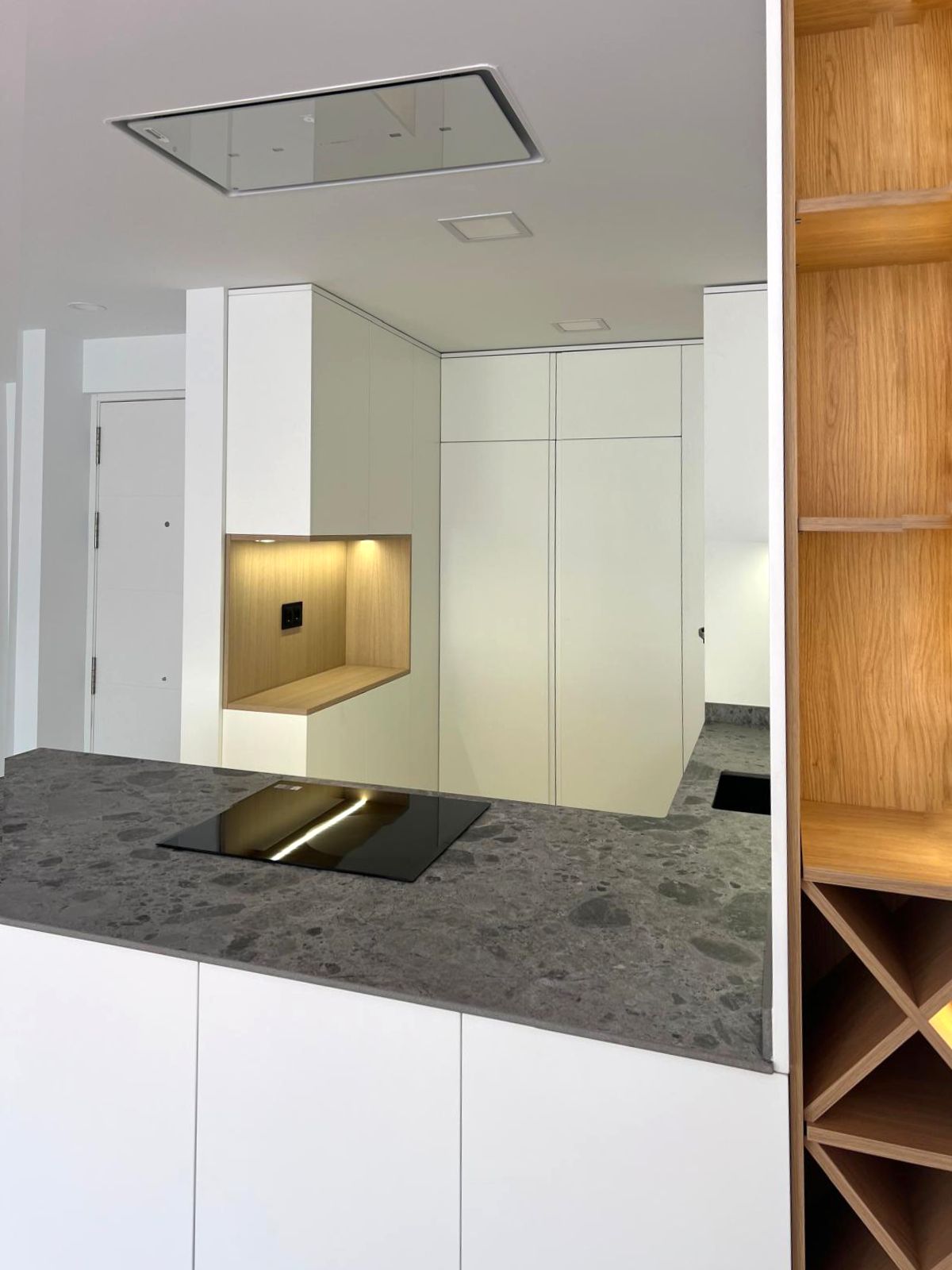 Detalle de encimera gris piedra con zona de cocción y mueble abierto en madera