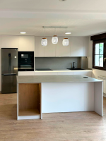 Vista general de cocina moderna con isla central, encimera gris y lámparas colgantes blancas.