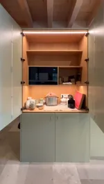 Detalle de estantería de madera integrada en muebles verdes de cocina.