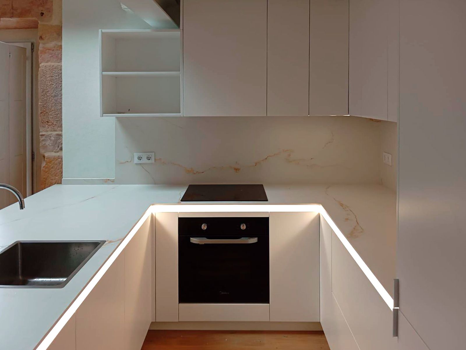 Cocina blanca moderna con encimera porcelánica y pared de piedra natural Soinco