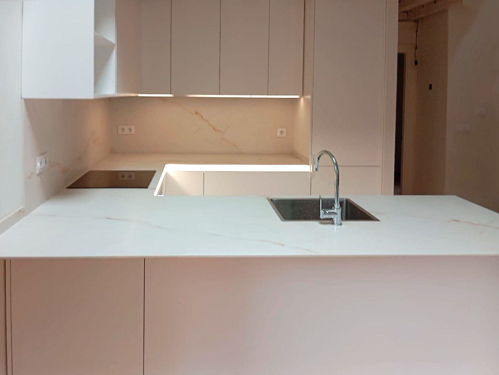 Cocina blanca moderna con encimera porcelánica efecto mármol y pared de piedra vista.