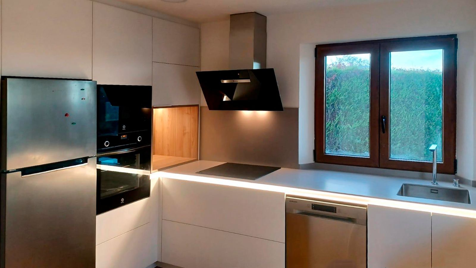 Cocina blanca con madera y luz natural en distribución en L diseñada por Soinco