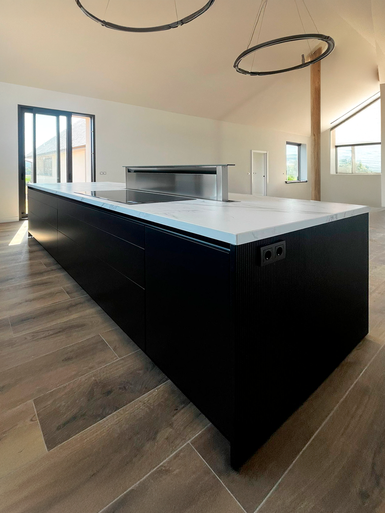 Detalle de isla de cocina negra con campana downdraft oculta y encimera de mármol blanco.
